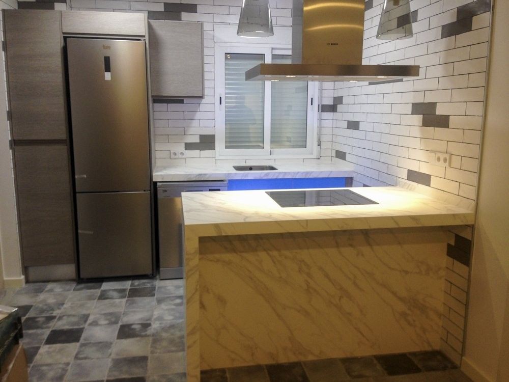 Cocina abierta con península imitación mármol y pared de metro blanco en Blasco Ibáñez