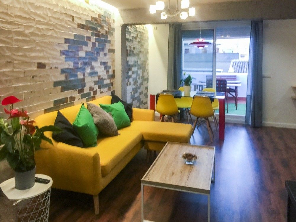 Salón con pared de plaqueta de colores y sofá amarillo en piso de Cullera
