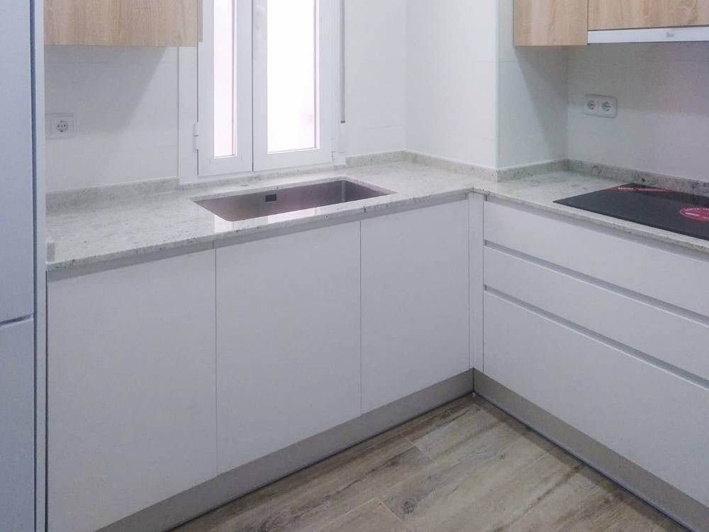 Cocina en L blanca sin tiradores con encimera de granito claro en Embajadores