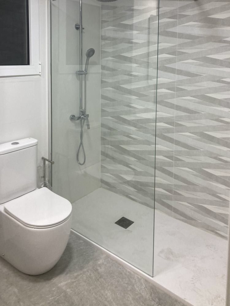 Baño con plato de ducha, mampara fija y paño de azulejo geométrico gris