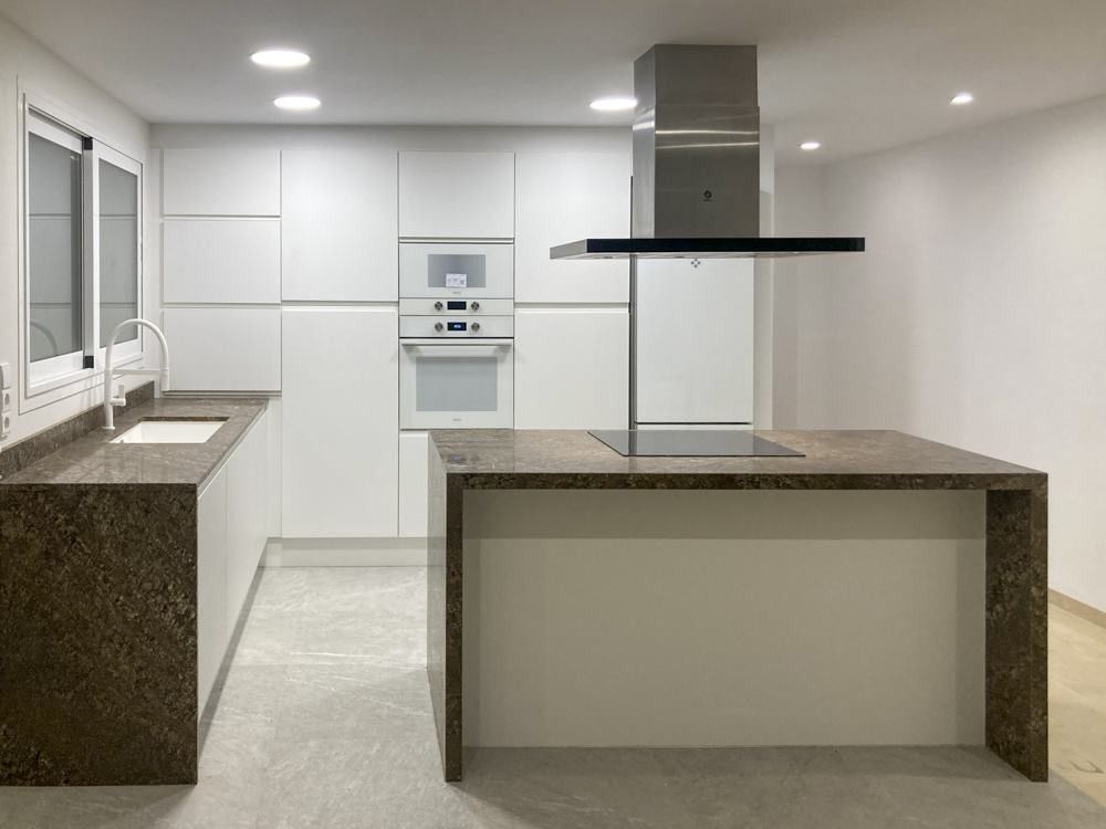 Cocina blanca con isla de granito y campana de acero en Navarro Reverter
