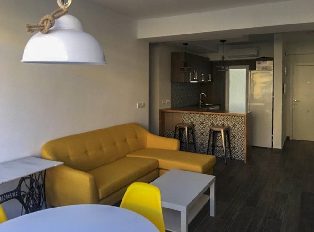 Salón con sofá mostaza y cocina abierta con barra en San Vicente Mártir