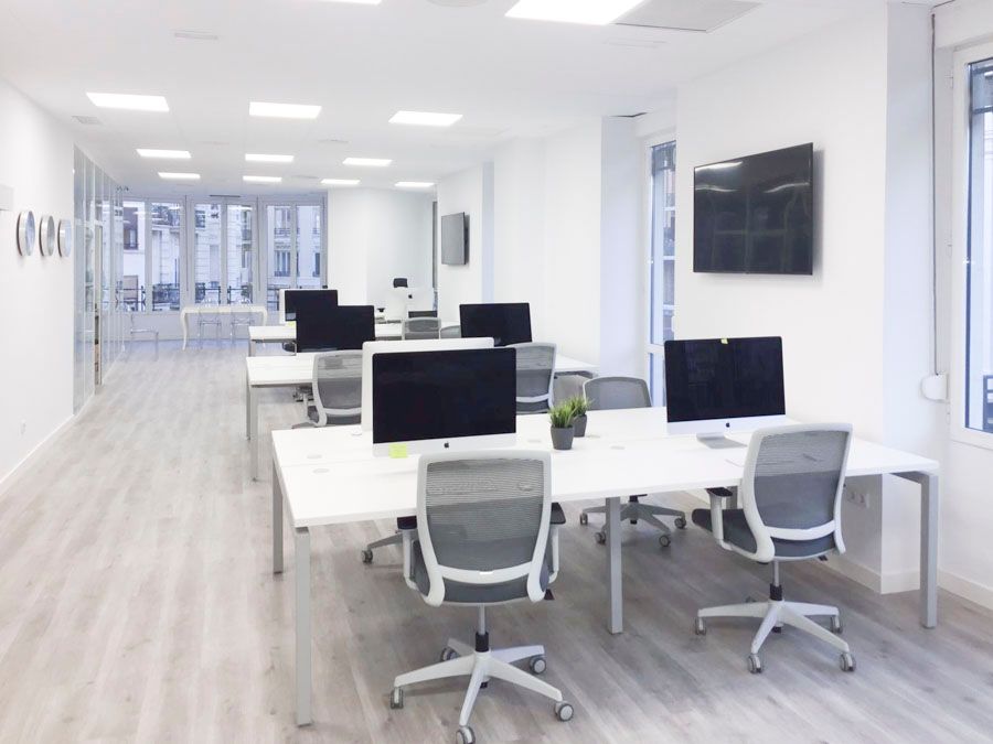 Zona de trabajo diáfana con mesas blancas y paneles LED en oficina de Valencia