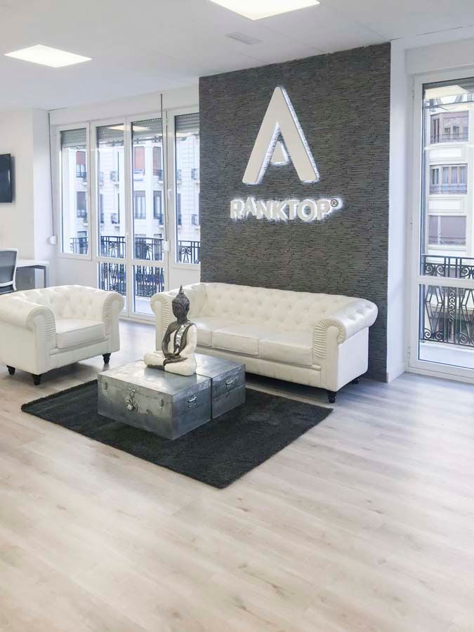 Recepción con pared de piedra oscura, logotipo corpóreo y sofás blancos