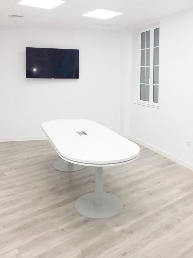 Sala de reuniones con mesa ovalada blanca y pantalla en la pared