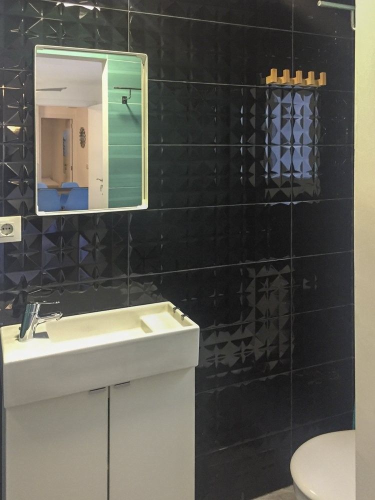 Lavabo con mueble blanco sobre alicatado negro de rombos en relieve