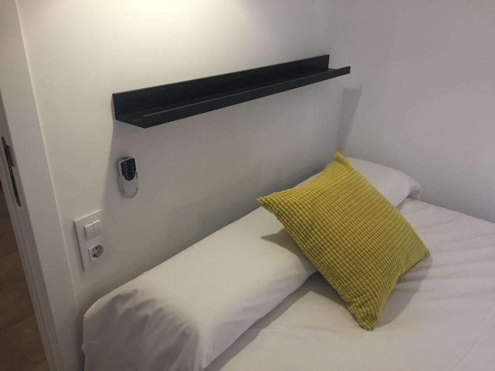Balda negra en el cabecero con enchufe e interruptor junto a la cama