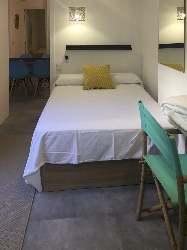 Dormitorio con cama de madera, silla verde y suelo porcelánico gris