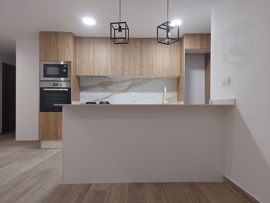 Cocina abierta con península blanca y lámparas de jaula negra en avenida Archiduque Carlos