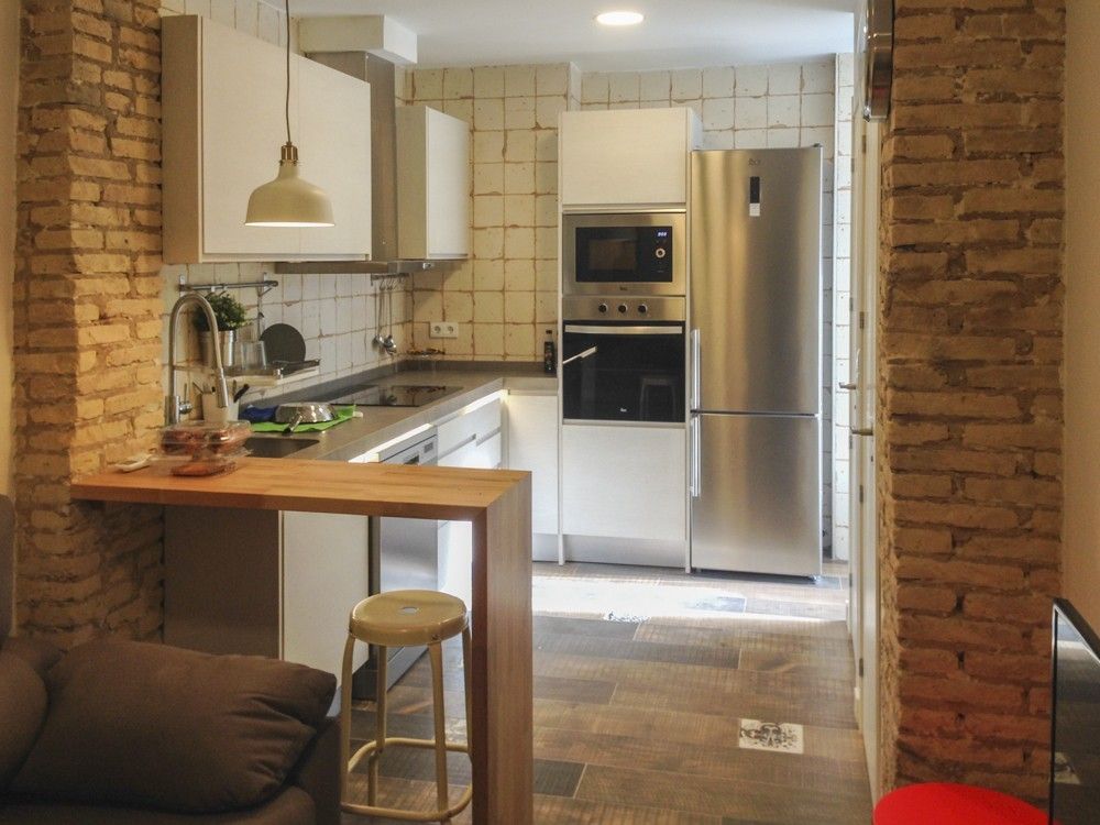 Cocina en L con barra de madera y ladrillo visto en Benimaclet