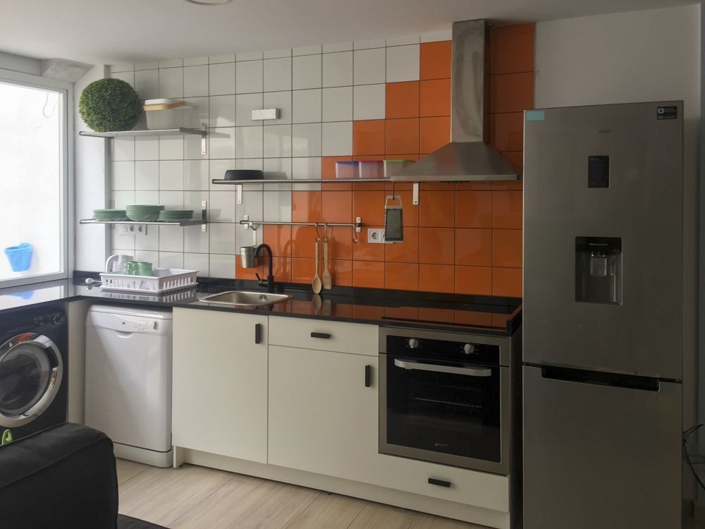 Cocina con muebles blancos y alicatado naranja en escalera en calle Dolores