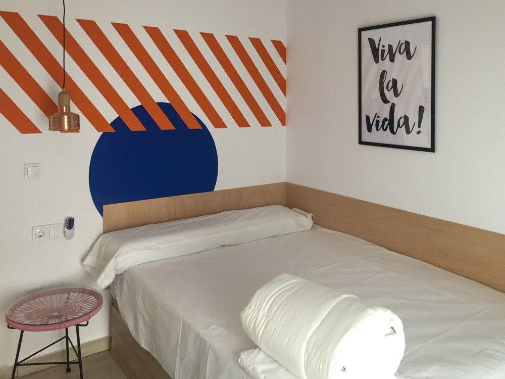 Dormitorio con franjas naranjas y círculo azul pintados en la pared del cabecero