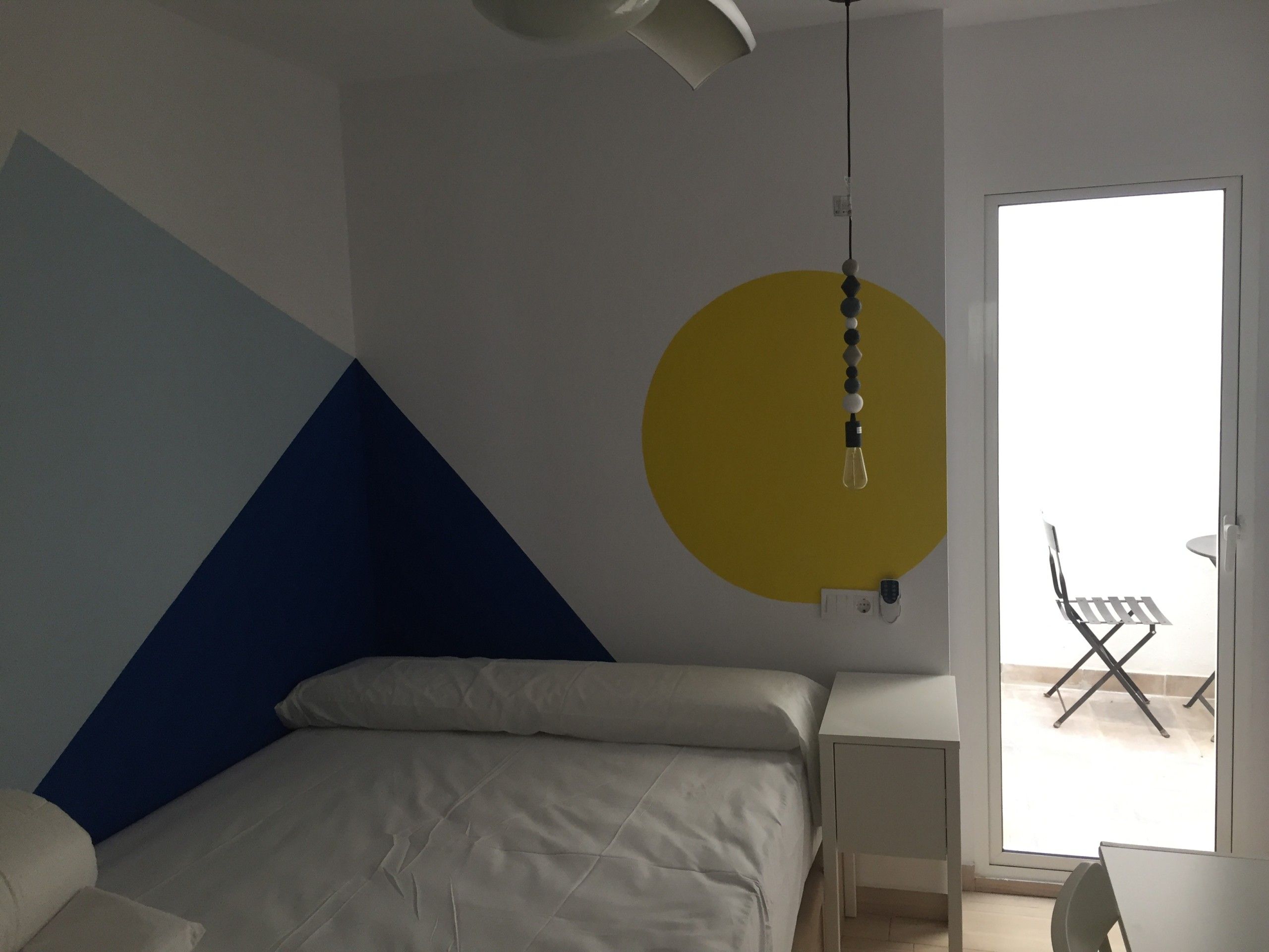 Dormitorio con triángulos azules y círculo amarillo pintados en la pared
