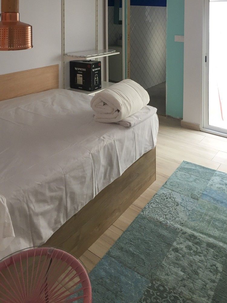 Cama con base de madera y alfombra turquesa en piso reformado de Valencia