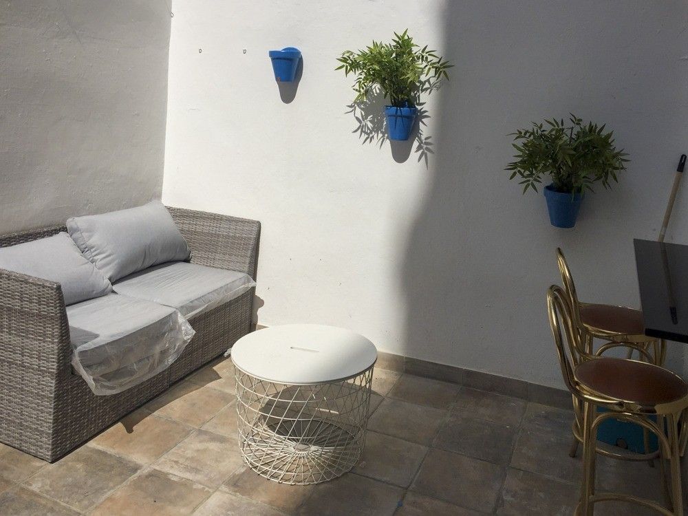 Patio con suelo de barro, sofá exterior y macetas azules en la pared