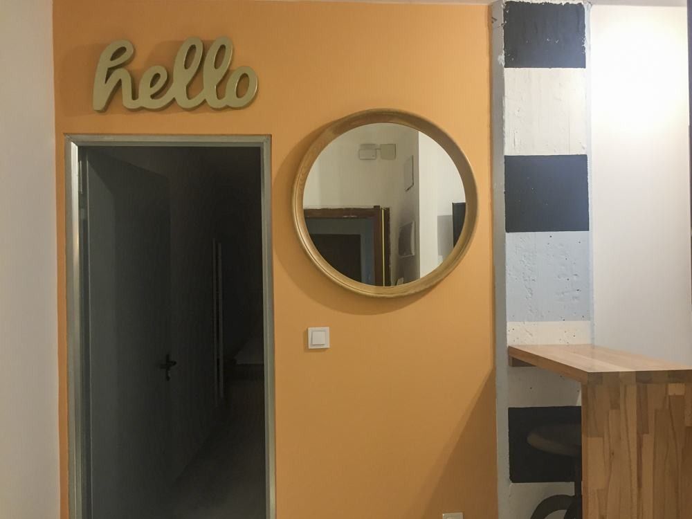 Recibidor con pared naranja y espejo redondo en piso de Valencia