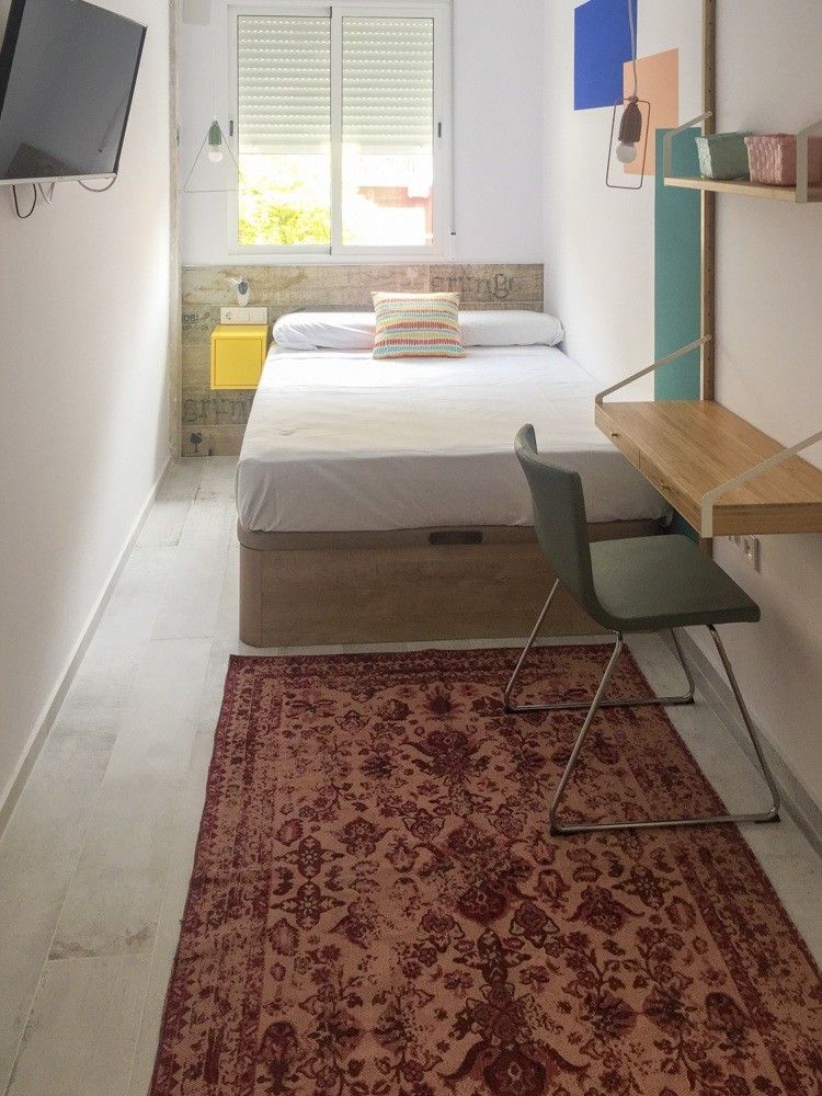 Dormitorio estrecho con cama, escritorio y alfombra roja