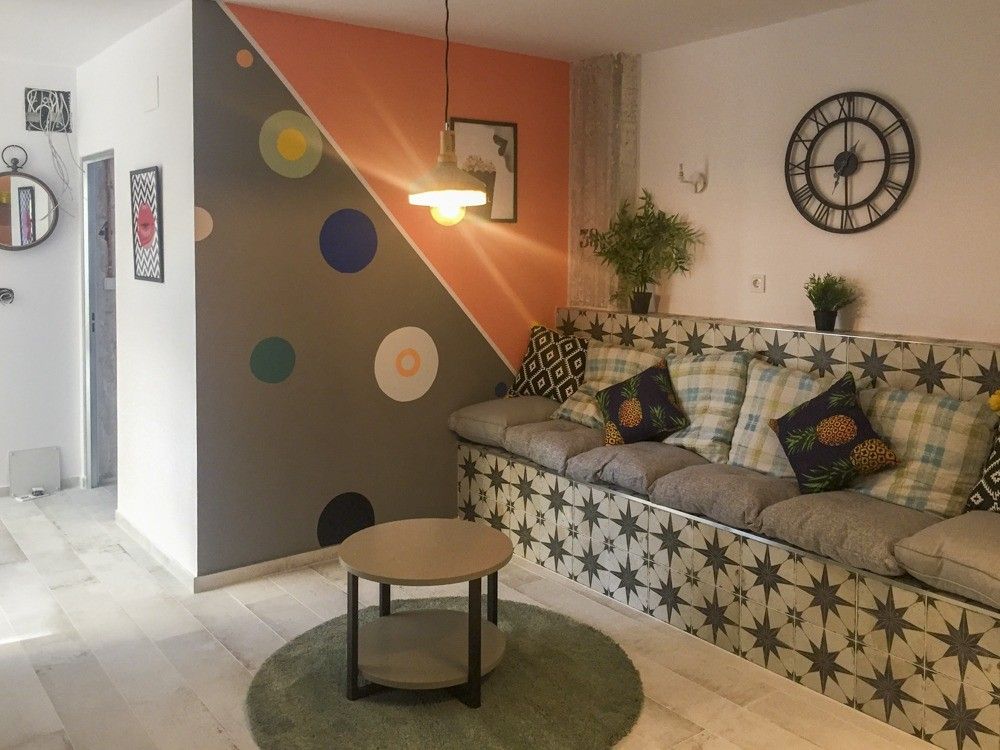 Salón con pared geométrica naranja y gris y banco de obra en calle Janini