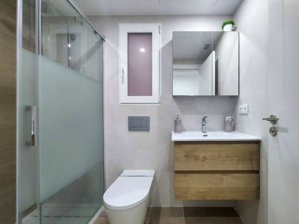 Baño con mampara, inodoro suspendido y mueble de lavabo de madera