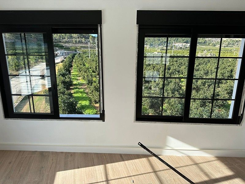 Habitación con ventanas de perfil negro abiertas a los campos de naranjos