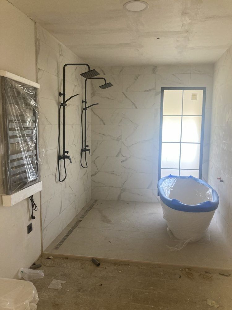 Baño en obra con bañera protegida, ducha y porcelánico imitación mármol