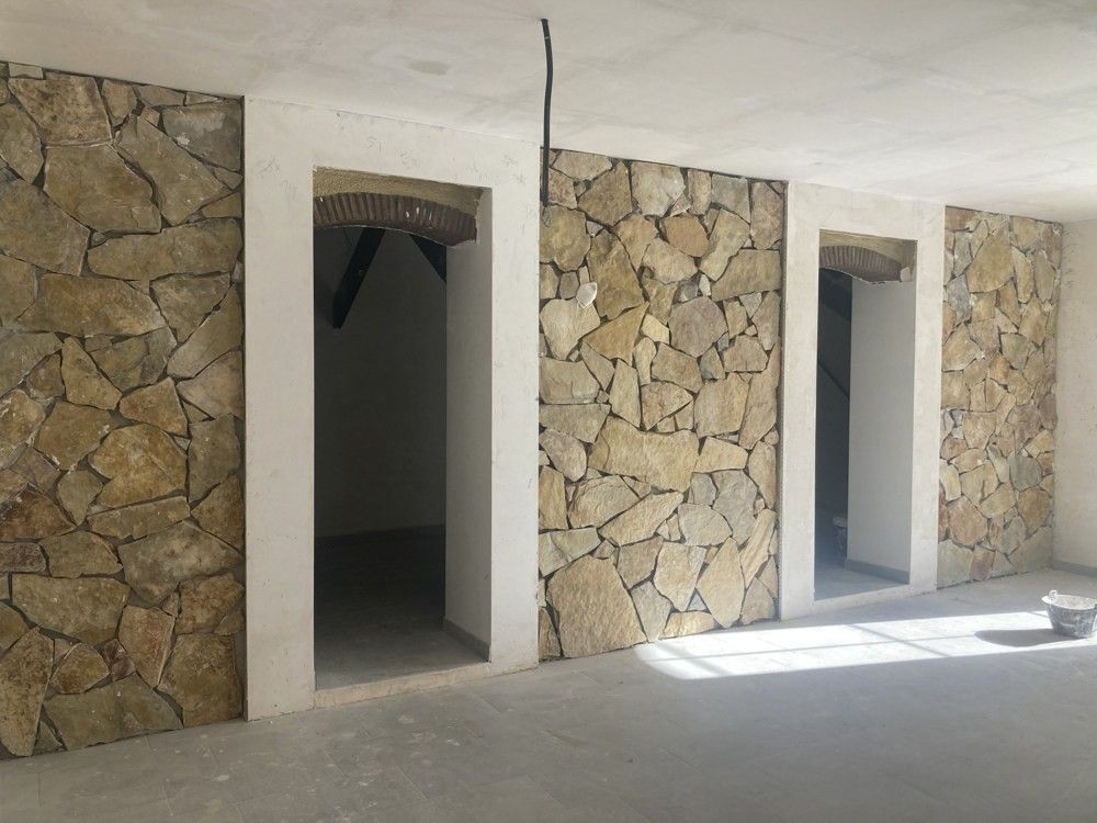 Estancia en obra con muros de piedra vista y huecos de paso nuevos